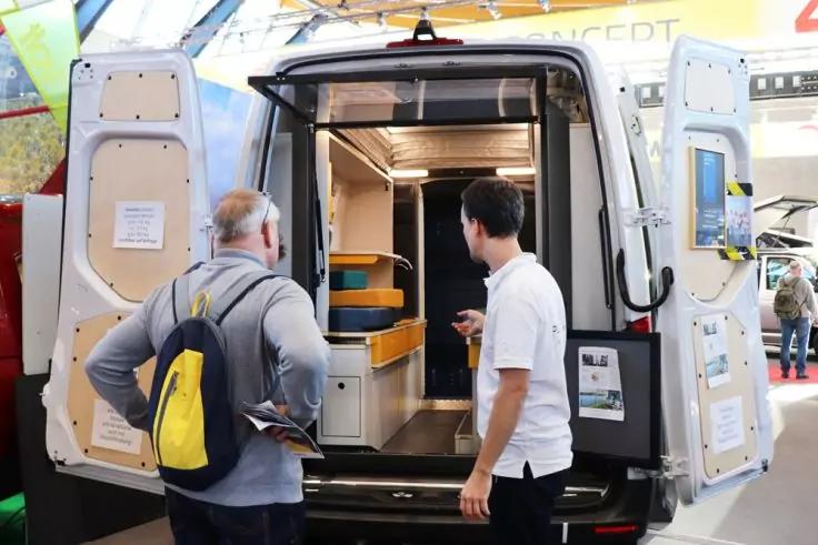 Offener Kastenwagen mit Regalen im Laderaum, zwei M&auml;nner stehen davor, einer zeigt ins Innere