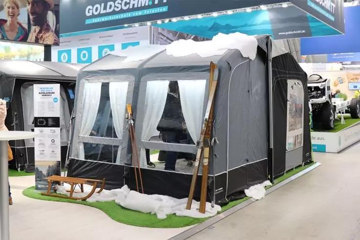 Graues Vorzelt mit wei&szlig;en Vorh&auml;ngen und Fenstern, h&ouml;lzerne Ski und Schlitten, k&uuml;nstlicher Schnee und gr&uuml;ner Kunstrasen in einer Messehalle