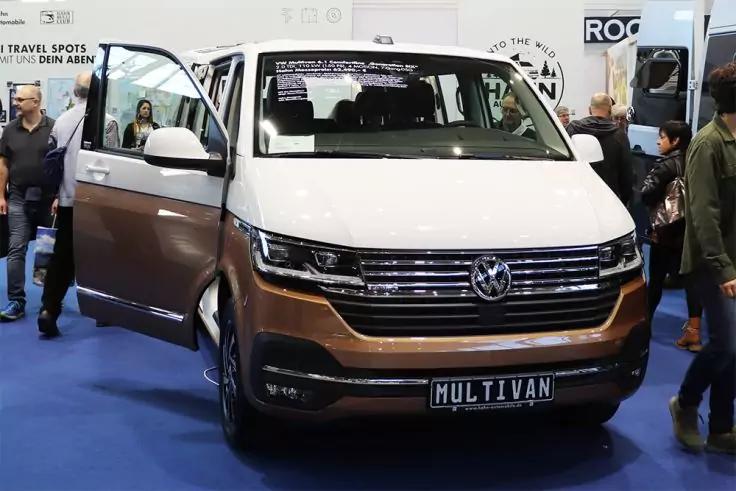 Frontansicht eines zweifarbigen Volkswagen Multivan mit ge&ouml;ffneter Seitent&uuml;r, Kennzeichen 'MULTIVAN', Menschen und St&auml;nde im Hintergrund