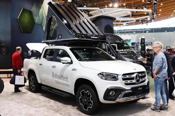 Wei&szlig;er Pickup mit ge&ouml;ffnetem Dachzelt auf einem Messestand, Personen stehen daneben