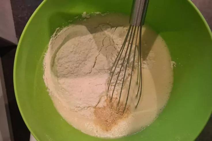 Gr&uuml;ne R&uuml;hrsch&uuml;ssel mit wei&szlig;em Pulver, hellem Fl&uuml;ssigkeitsfilm, einem Metallquirl und einem kleinen Haufen beige K&ouml;rner am Rand