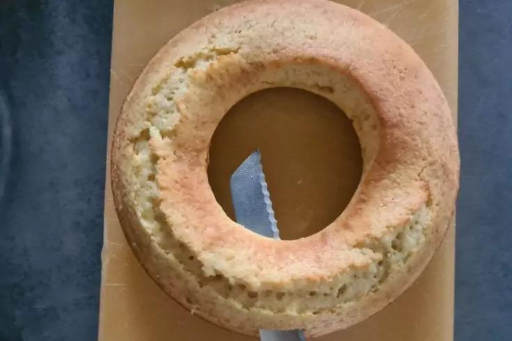 Ringf&ouml;rmiger Kuchen mit rissiger Oberfl&auml;che auf einem rechteckigen Holzbrett, gezacktes Messer steckt in der Mitte