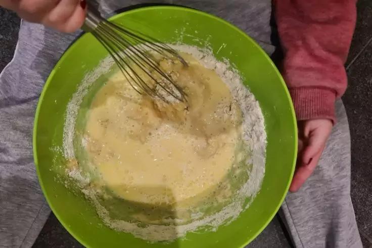 Zwei H&auml;nde halten einen Schneebesen &uuml;ber einer gr&uuml;nen Sch&uuml;ssel mit Teig