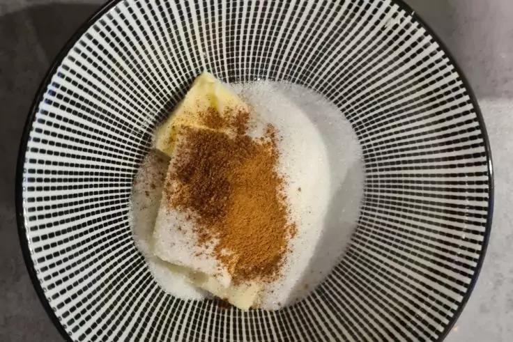 Schwarze Schale mit feinem Linienmuster, darin ein gelbes rechteckiges St&uuml;ck auf wei&szlig;em Schaum, bestreut mit braunem Pulver