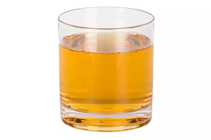 Transparentes Trinkglas mit bernsteinfarbener Fl&uuml;ssigkeit, halbvoll, auf wei&szlig;em Hintergrund