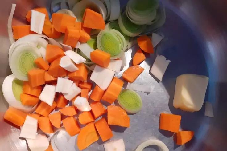 Gehackte Karottenw&uuml;rfel, Lauchringe und ein St&uuml;ck Butter in einem Metalltopf