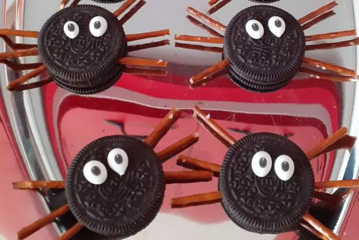 Vier runde Schokoladen-Sandwichkekse, jeder mit zwei wei&szlig;en Zuckergussaugen und d&uuml;nnen braunen St&auml;bchen rundherum, auf einem silbernen Tablett mit rotem Hintergrund