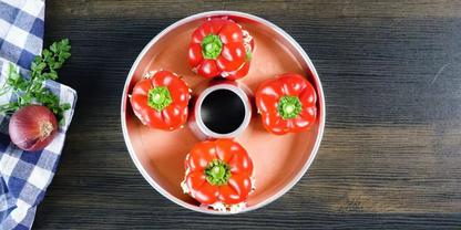 Draufsicht auf vier rote Paprika in einer runden Form um eine kleine Schale mit dunkler Fl&uuml;ssigkeit, auf dunklem Holztisch; links kariertes K&uuml;chentuch, rote Zwiebel und Petersilie