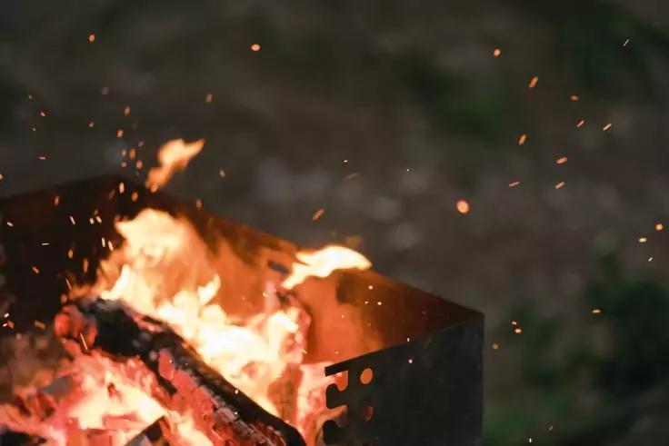 Brennendes Feuer in einer rechteckigen Metallfeuerstelle mit gl&uuml;henden Holzscheiten und Funken