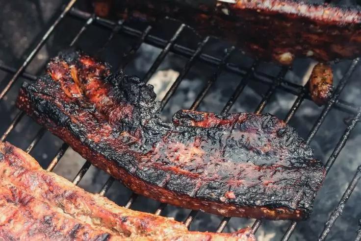 St&uuml;ck gegrilltes Fleisch mit dunklen verkohlten Stellen auf einem Grillrost