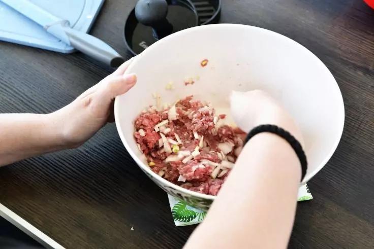 H&auml;nde mischen Hackfleisch und gehackte Zwiebeln in einer wei&szlig;en Sch&uuml;ssel auf einem dunklen Tisch