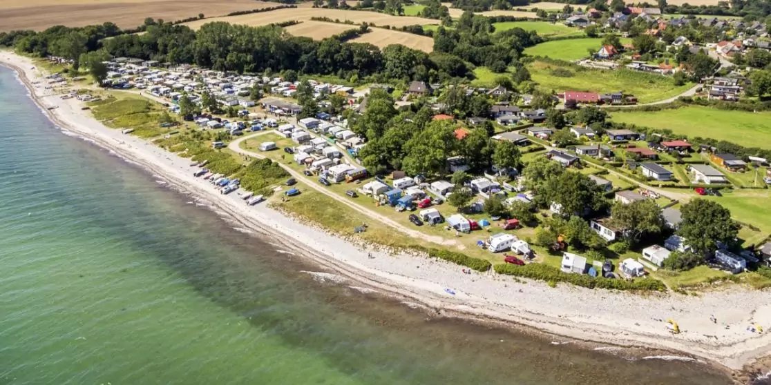 Luftaufnahme einer K&uuml;ste mit Strand, gr&uuml;nlichem Meer, Reihen von H&auml;usern und Wohnwagen, B&auml;umen und Feldern