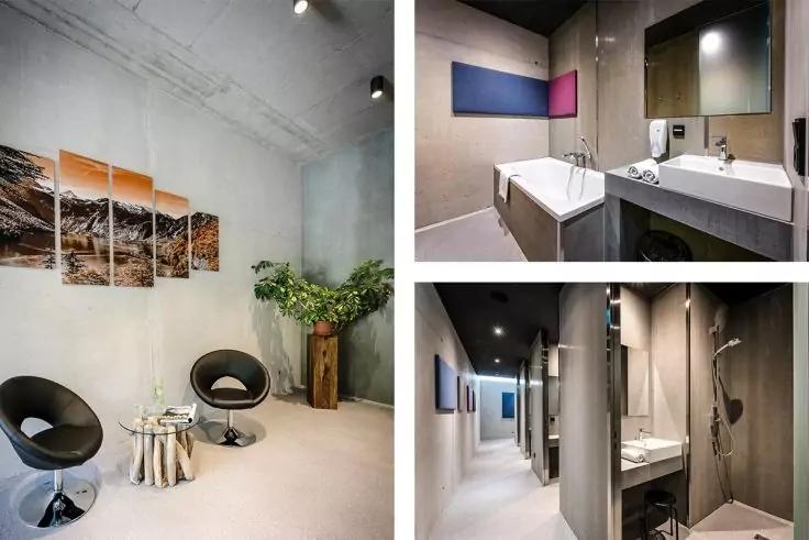 Links zwei schwarze runde Stühle, kleiner Metallbeistelltisch, mehrteiliges Wandbild in Braun- und Orangetönen und Topfpflanze; rechts oben Badewanne, zwei Waschbecken, Spiegel und Waschmaschine; rechts unten Duschbereich, Waschbecken, Spiegel und be