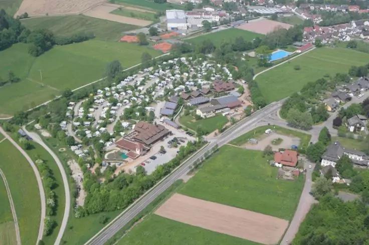 Luftaufnahme eines Gebiets mit vielen weißen Wohnwagen oder Mobilheimen, mehreren Gebäuden, einem rechteckigen blauen Pool, Straßen, Feldern und Bäumen