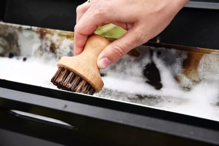 Hand h&auml;lt eine Holzb&uuml;rste &uuml;ber einer schaumigen Metallwanne