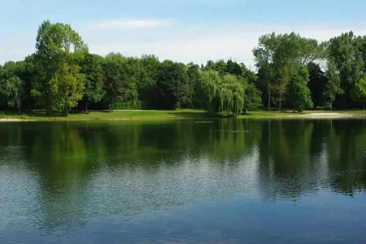 See mit B&auml;umen am Ufer, Spiegelung der B&auml;ume im Wasser und blauer Himmel