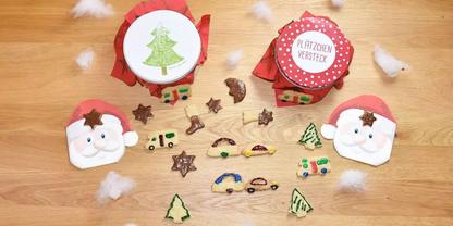 Zwei runde rote Dosen mit dekorativen Deckeln, zwei Papierumschl&auml;ge mit Weihnachtsmann-Gesichtern, mehrere kleine Holzfiguren (Sterne, Tannen, Autos) und Baumwollflaum auf einer Holzoberfl&auml;che