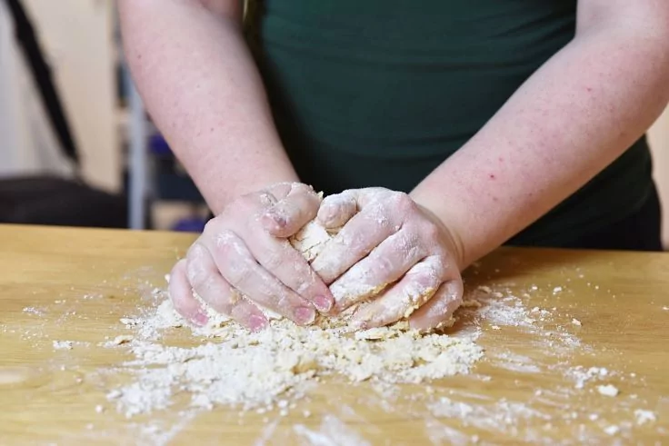 Hände kneten Teig auf einer bemehlten Holzarbeitsfläche