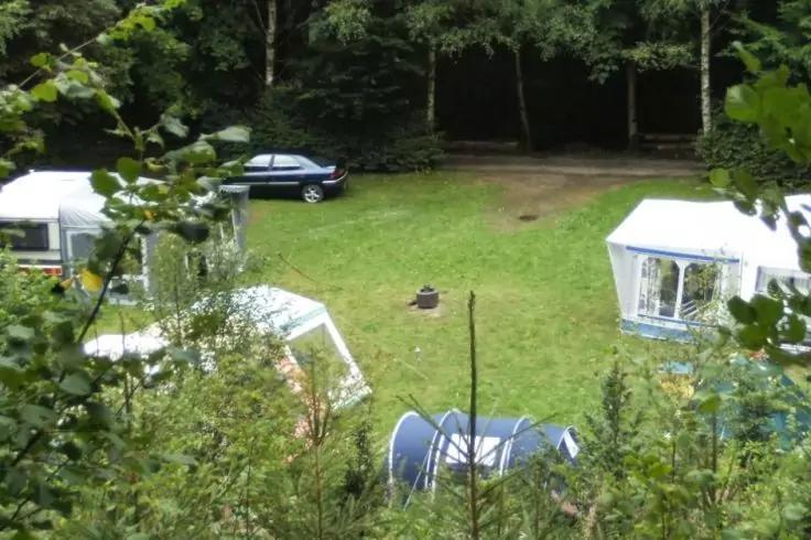 Wiese mit zwei wei&szlig;en Pavillons, einem blauen Zelt, zwei Wohnwagen, einem schwarzen Auto und B&auml;umen im Hintergrund