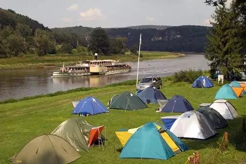 Mehrere Zelte auf einer Wiese am Fluss; Raddampfer auf dem Wasser, Pkw, B&auml;ume und Felsen im Hintergrund