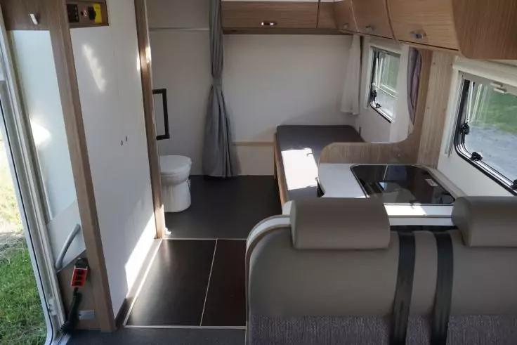 Innenraum eines Wohnmobils mit Sitzbank, K&uuml;chenzeile (Sp&uuml;le, Kochfeld), Fenstern, Oberschr&auml;nken und offener Toilette mit Vorhang