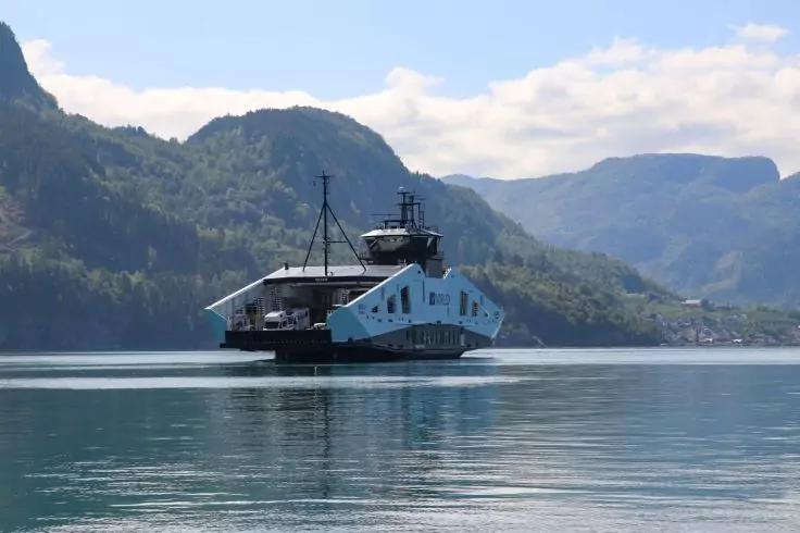 F&auml;hre auf ruhigem Wasser, im Hintergrund Berge und bew&ouml;lkter Himmel