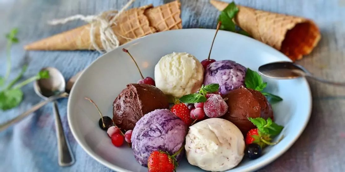 Teller mit mehreren Eiskugeln in verschiedenen Farben, Erdbeeren, kleinen roten Beeren, Minzbl&auml;ttern, zwei Eiswaffeln und zwei L&ouml;ffeln