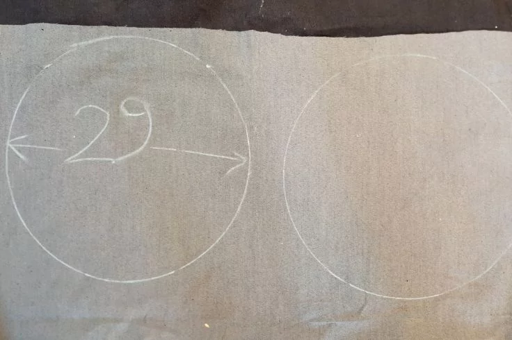 Zwei mit weißer Kreide auf grauem Stoff gezeichnete Kreise; im linken Kreis die Zahl "29" und ein horizontaler Doppelpfeil
