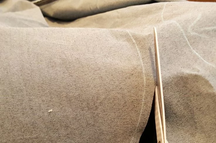 Schere schneidet dunkelgrauen Stoff entlang weißer Markierlinien