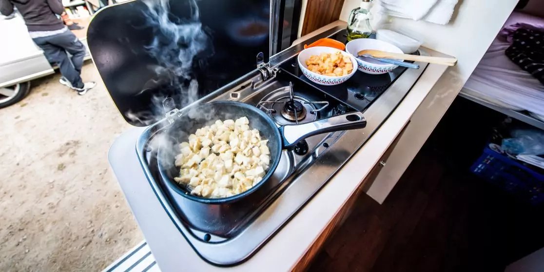 Zweiflammiger Gasherd in einer K&uuml;chenzeile: Bratpfanne mit dampfenden Teigst&uuml;cken, daneben Sch&uuml;ssel mit orangefarbener Beilage und Essst&auml;bchen