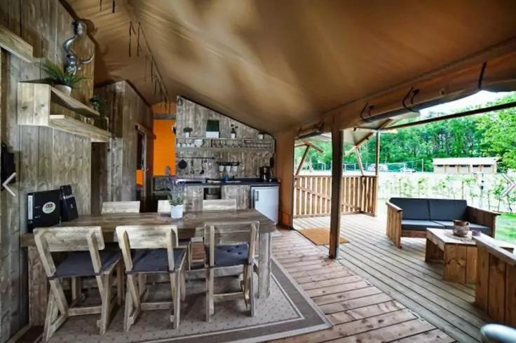 &Uuml;berdachte Holzterrasse mit Esstisch und St&uuml;hlen, offener K&uuml;chenzeile, Sitzbank und Gartenblick