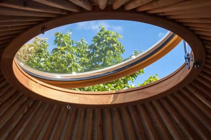 Runde &Ouml;ffnung im Dach mit Holzrahmen und radi&auml;ren Holzlatten, blauer Himmel und gr&uuml;ne Baumbl&auml;tter sichtbar