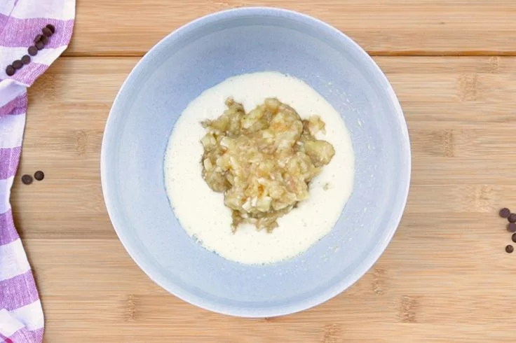 Hellblaues Sch&auml;lchen auf Holzbrett mit wei&szlig;er Sauce und einem Haufen braun-gr&uuml;ner Paste in der Mitte; links lila-wei&szlig;es Tuch und vereinzelte Pfefferk&ouml;rner