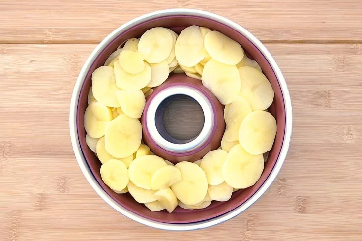 Runde Backform mit Loch in der Mitte, innen mit dünnen Kartoffelscheiben ringsherum auf Holzuntergrund