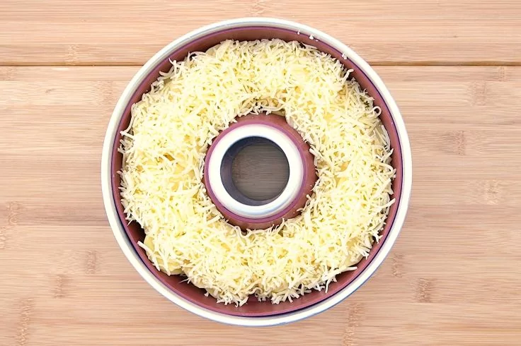 Draufsicht auf eine ringförmige Backform, gefüllt mit geriebenem Käse auf Holzuntergrund