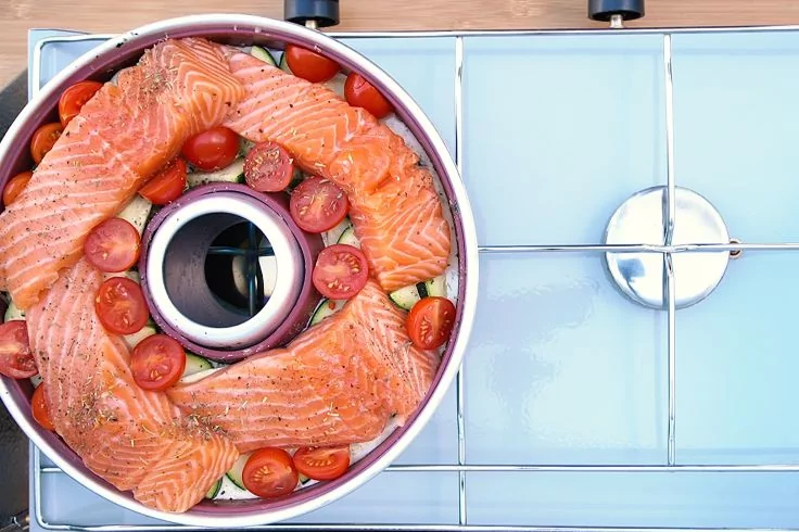 Runde Backform mit Loch in der Mitte auf dem Kochfeld, gefüllt mit rohen Lachsfilets und halbierten Cherrytomaten