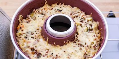 Runde Rohrkuchenform mit Innenrohr, gef&uuml;llt mit einer Mischung aus kleinen St&uuml;cken und mit geschmolzenem, geriebenem K&auml;se &uuml;berbacken, auf einem Herd