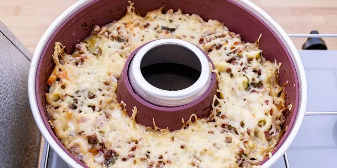 Runde Rohrkuchenform mit Innenrohr, gef&uuml;llt mit einer Mischung aus kleinen St&uuml;cken und mit geschmolzenem, geriebenem K&auml;se &uuml;berbacken, auf einem Herd