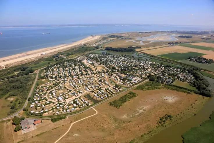 Luftaufnahme eines Campingplatzes mit vielen Wohnwagen, Strand, Meer und Feldern