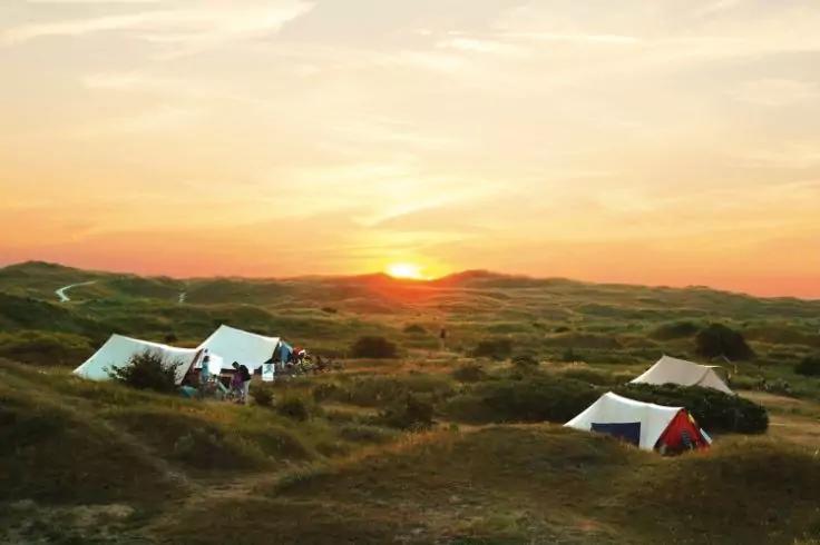 Zelte auf grasigen D&uuml;nen bei Sonnenuntergang, Personen neben einem der Zelte