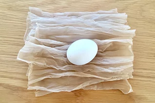 Wei&szlig;es Ei auf mehreren geschichteten, durchscheinenden wei&szlig;en Lagen auf heller Holzoberfl&auml;che