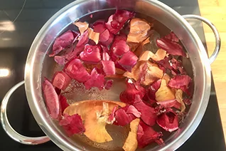 Edelstahltopf auf Herd mit Wasser und roten sowie braunen Zwiebelh&auml;uten, zwei Griffe sichtbar