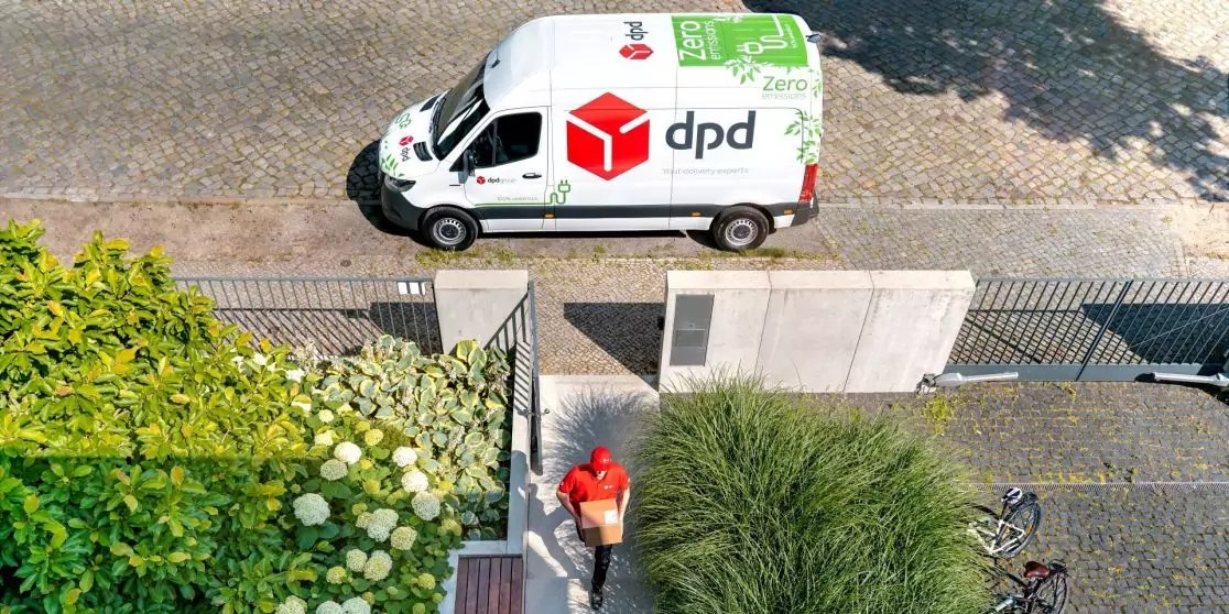 Blick von oben auf einen wei&szlig;en DPD-Transporter auf der Stra&szlig;e; eine Person in rotem Shirt tr&auml;gt ein Paket und geht eine Treppe zwischen Pflanzen hoch; Fahrradreifen am Rand