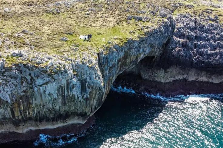 Meeresk&uuml;ste mit steiler Felsklippe und &Ouml;ffnung einer Meeresh&ouml;hle, grasbewachsene Klippenkante, Wellen am Felsfu&szlig;