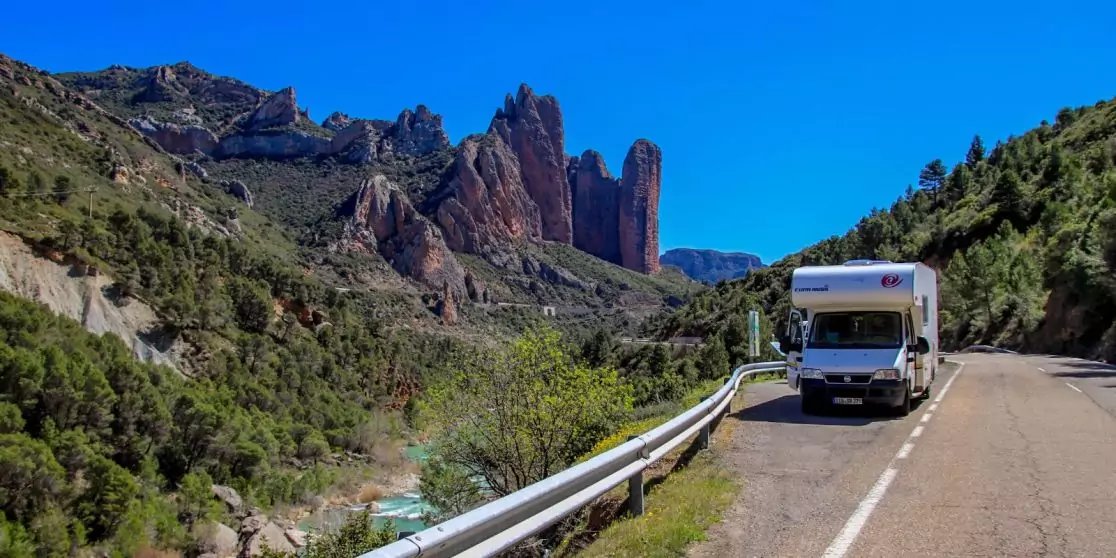 Wei&szlig;es Wohnmobil am Stra&szlig;enrand, links ein Fluss, im Hintergrund rote Felsformationen und blauer Himmel