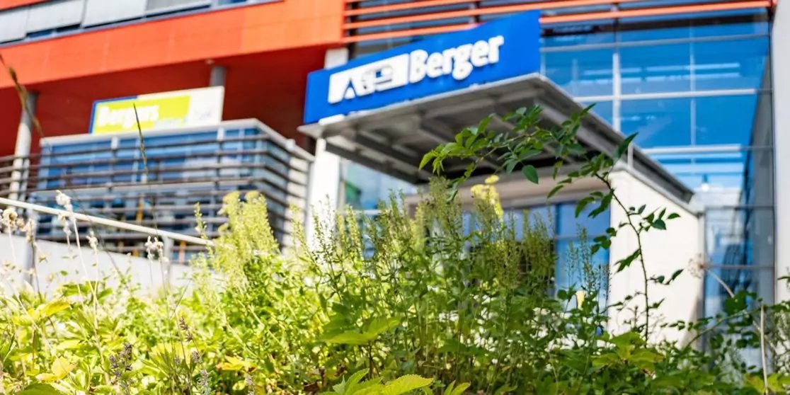 Gr&uuml;ne B&uuml;sche im Vordergrund, Glaseingang eines Geb&auml;udes, blaues Schild mit wei&szlig;er Aufschrift