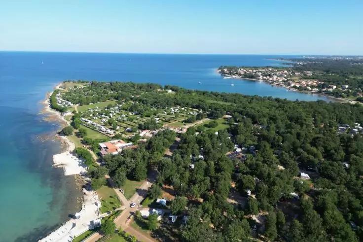 K&uuml;ste mit Meer, Sandstrand, Wohnh&auml;usern und bewaldeten Fl&auml;chen unter klarem Himmel