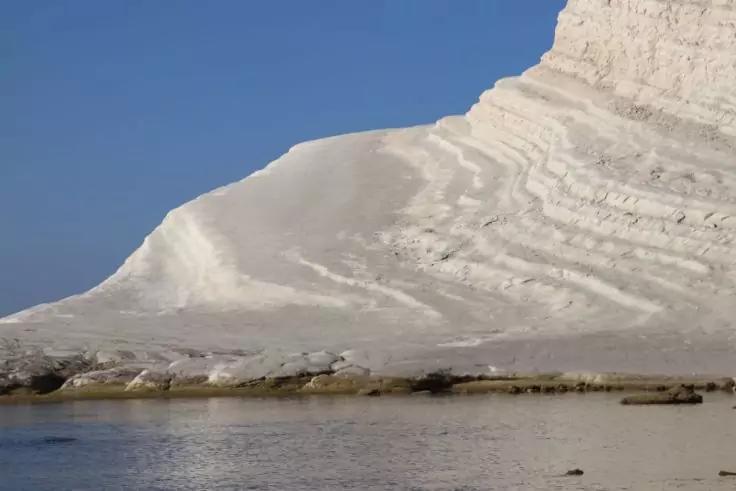 Wei&szlig;e, geschichtete Felswand am Meer unter blauem Himmel, ruhiges Wasser im Vordergrund