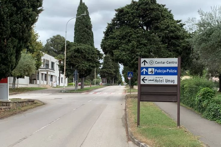 Stra&szlig;e mit Wegweiser 'Centar-Centro', 'Policija-Polizia', 'Hotel Umag', Gehweg, Zebrastreifen und B&auml;ume