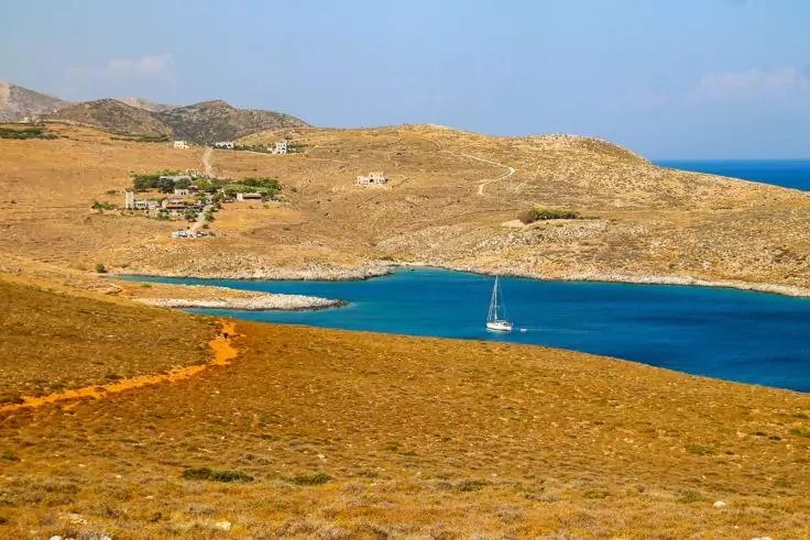 Bucht mit blauem Wasser, Segelboot, trockene braune H&uuml;gel, vereinzelte Geb&auml;ude und schmaler Erdweg